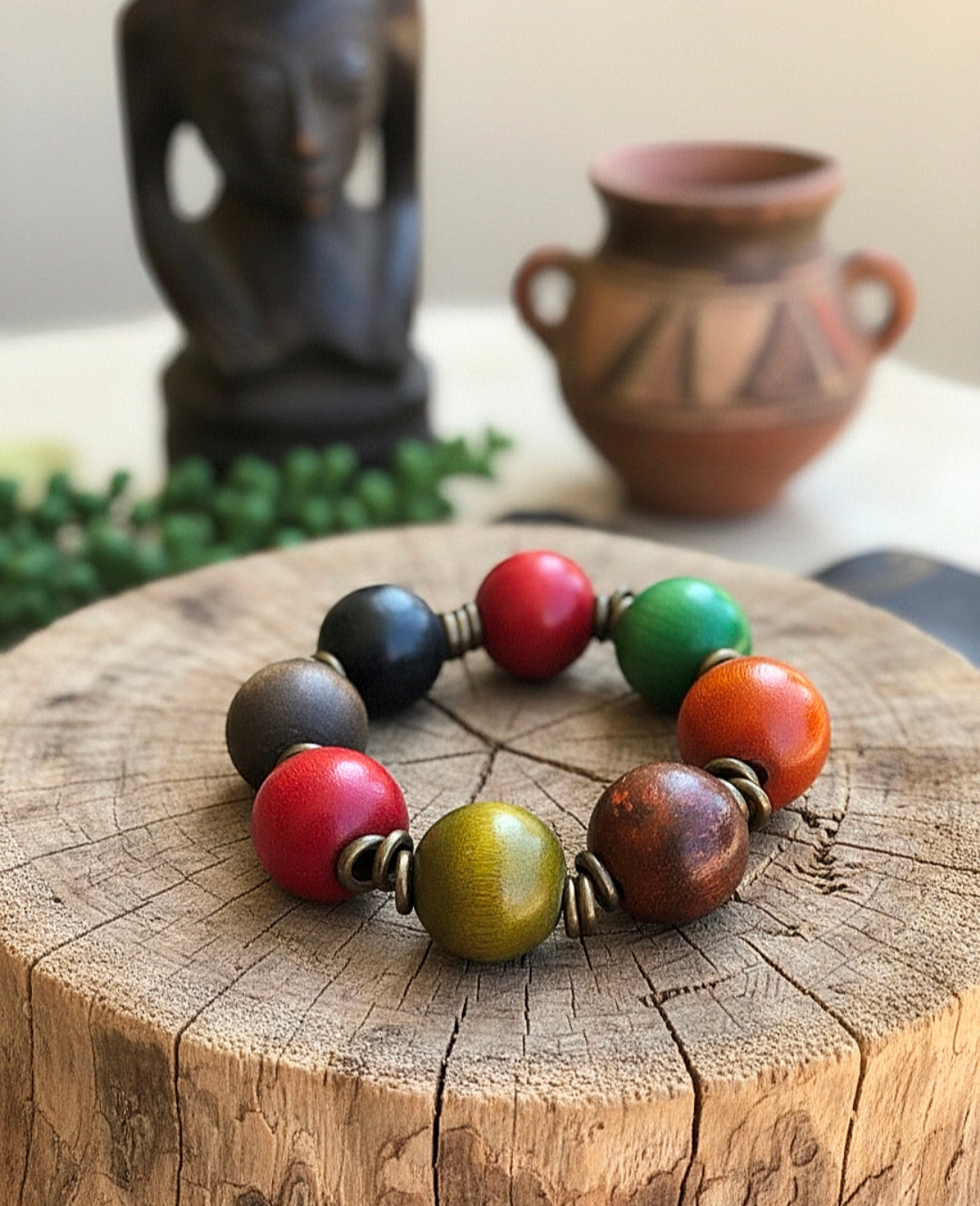 Colorful beaded bracelet on a wooden surface with a decorative vase and statue in the background.