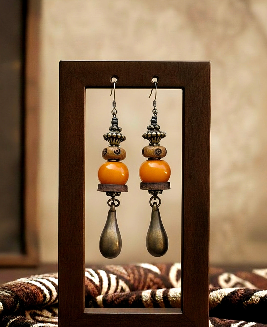 Pair of earrings with orange and brown beads in a wooden frame.