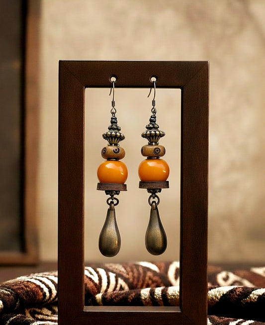 Pair of earrings with orange and brown beads in a wooden frame.