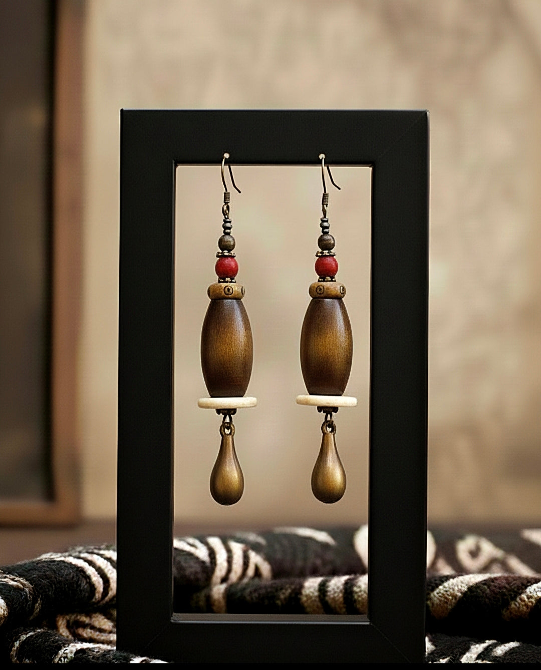 Pair of wooden earrings displayed in a black frame against a neutral background