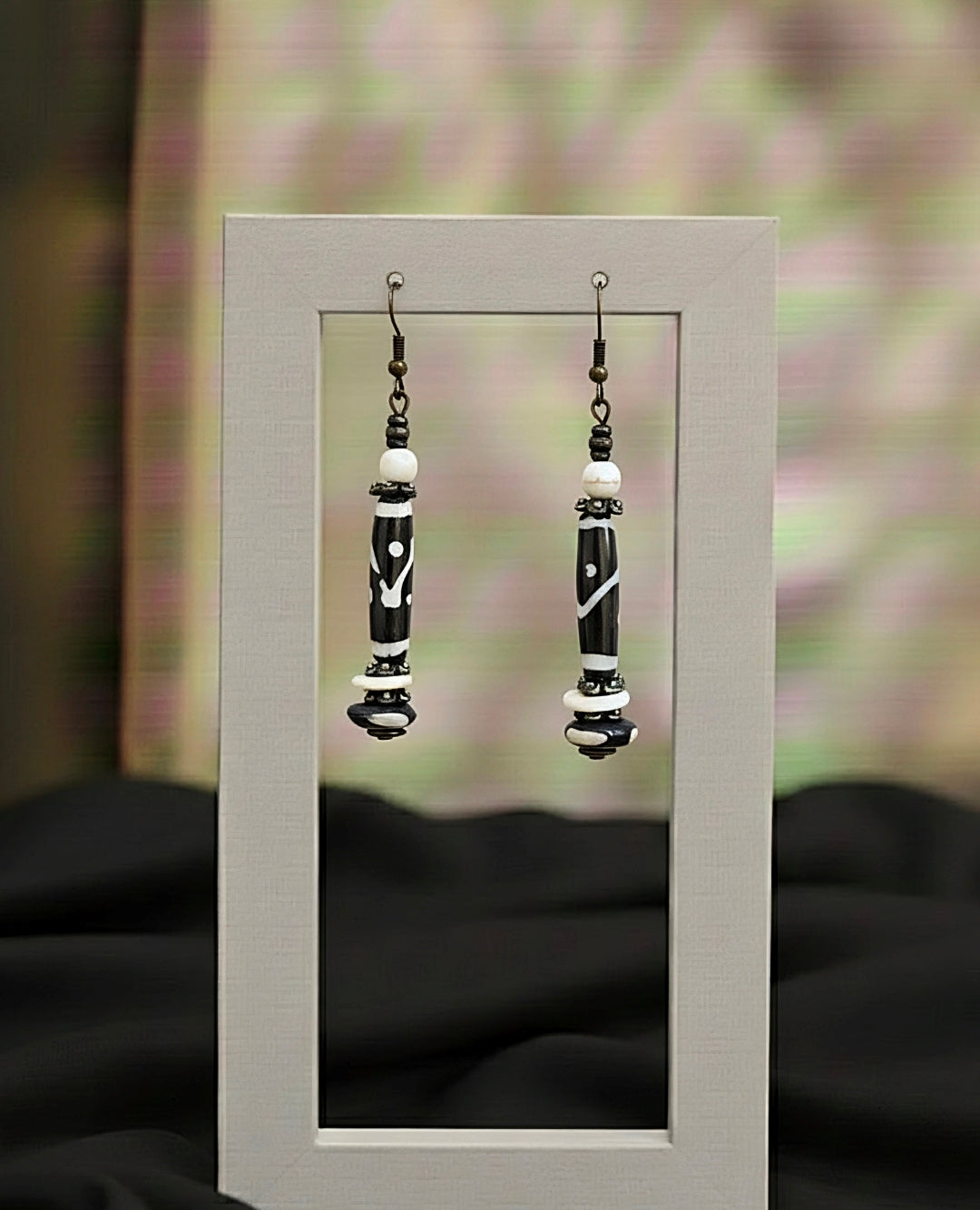 Black and white beaded earrings displayed in a small mirror with a blurred floral background.