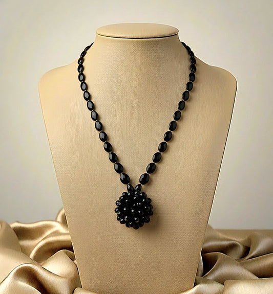 Black beaded necklace on a mannequin bust with beige fabric background