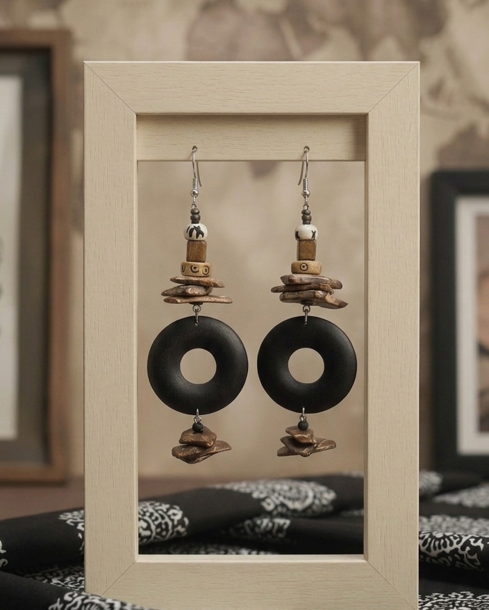 Pair of earrings with black circular pendants and cork-like elements on a beige display card.