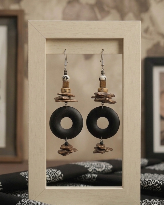 Pair of earrings with black circular pendants and cork-like elements on a beige display card.