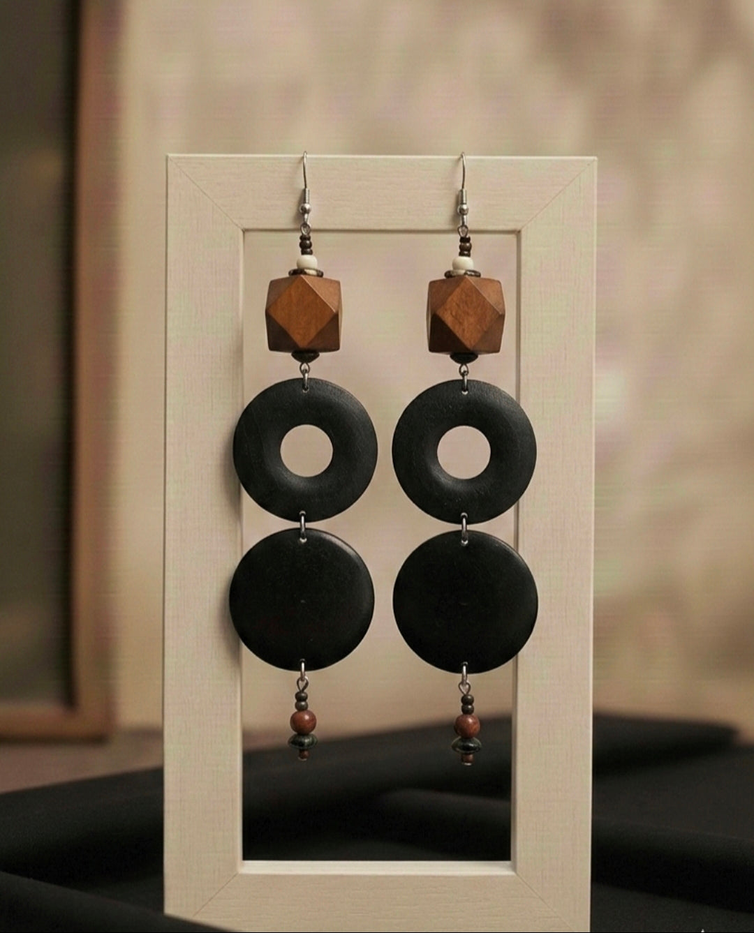 Pair of earrings with black circular pendants and wooden accents on a display card.