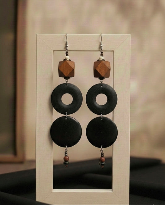 Pair of earrings with black circular pendants and wooden accents on a display card.