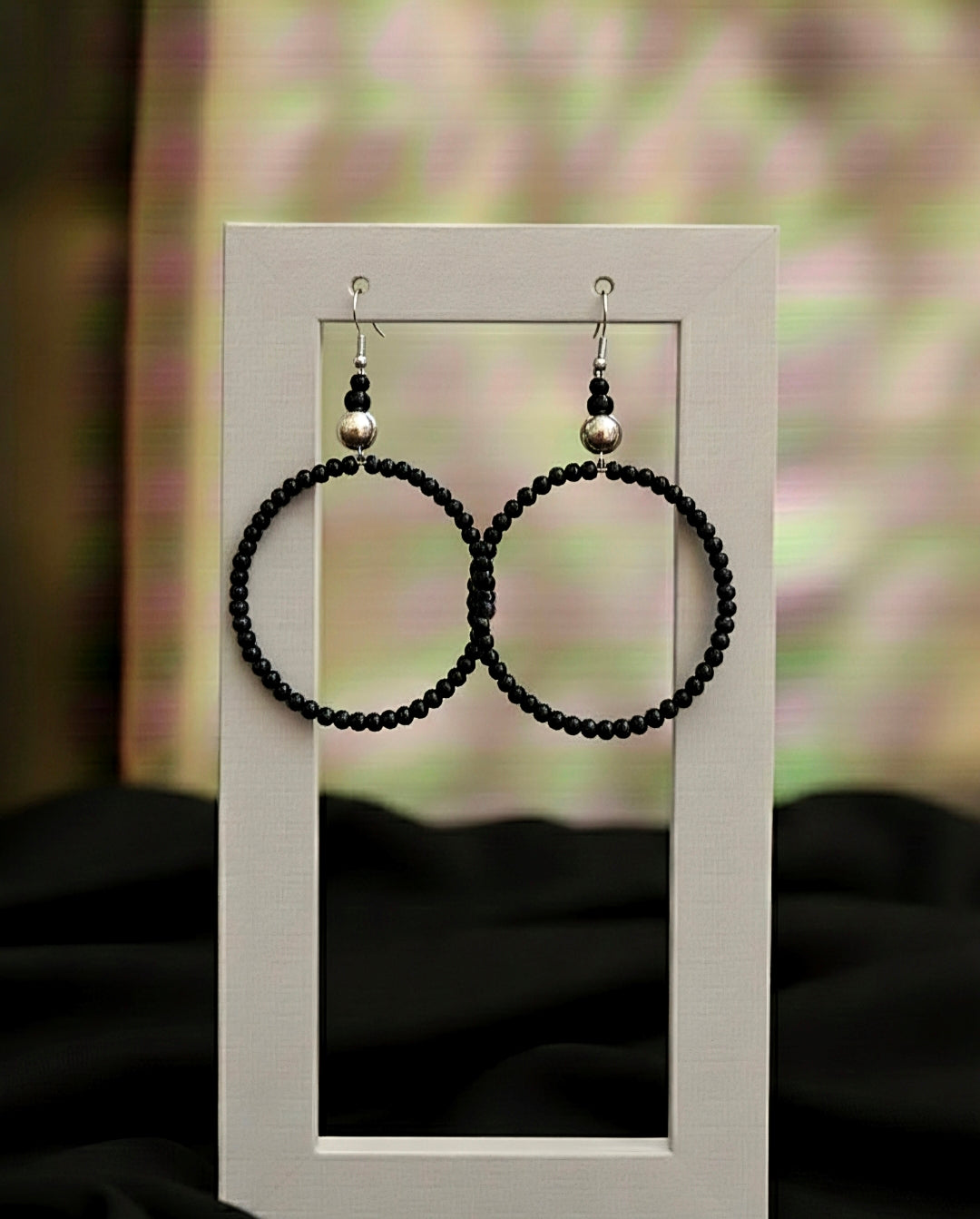 Black beaded hoop earrings on a white stand with a blurred background