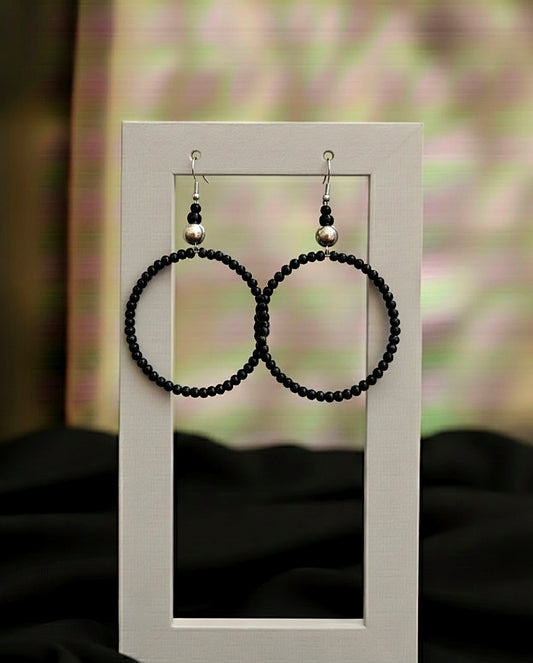Black beaded hoop earrings on a white stand with a blurred background