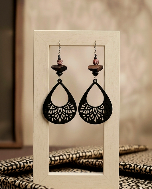 Pair of black earrings with wooden accents on a white frame against a blurred background