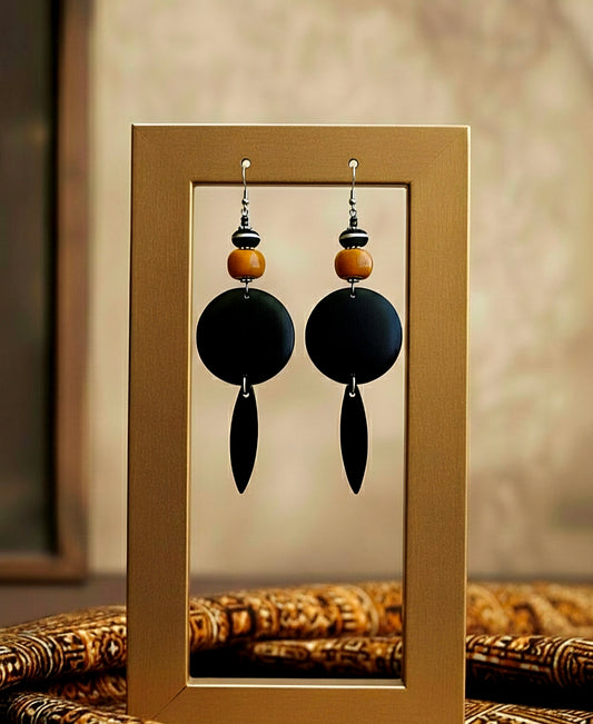 Pair of black earrings with wooden beads displayed in a gold frame.