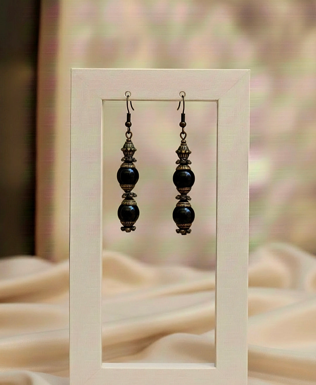 Pair of black beaded earrings displayed in a white frame against a blurred background