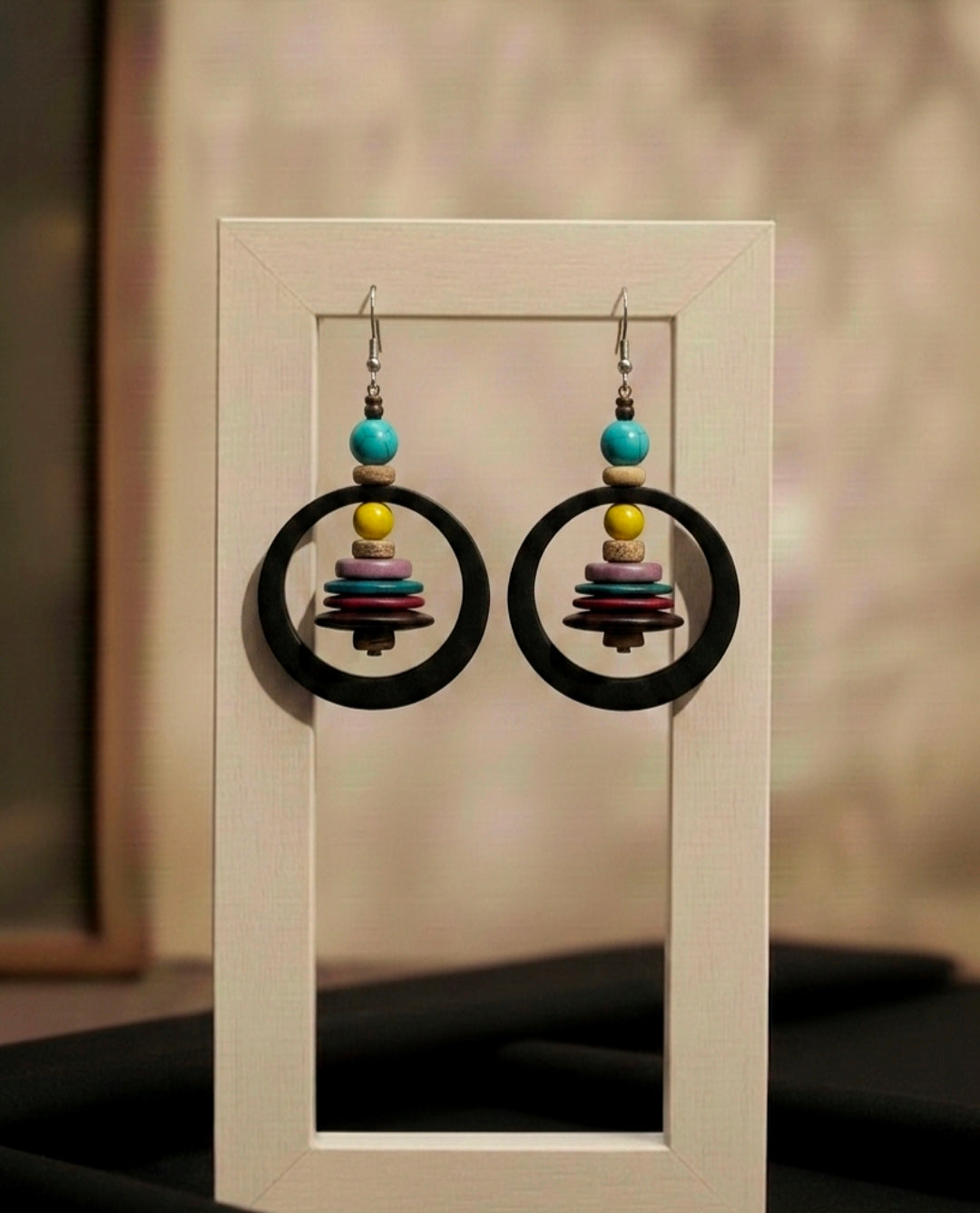 Pair of earrings with colorful beads in a black circular design on a neutral background
