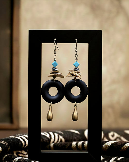 Pair of earrings with black rings, gold accents, and turquoise stones on a display card.