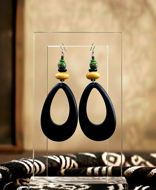 Pair of black earrings with green and yellow accents on a clear stand.