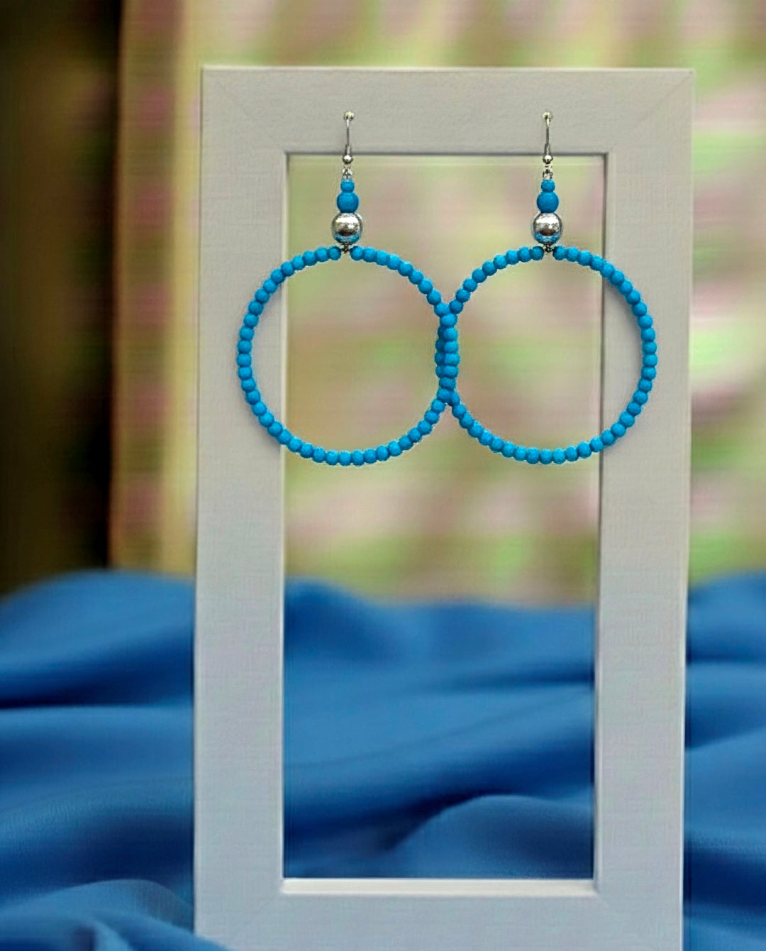 Blue beaded hoop earrings on a white card with a blurred blue fabric background