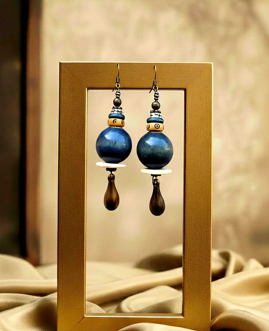 Pair of blue beaded earrings with gold accents on a reflective surface.
