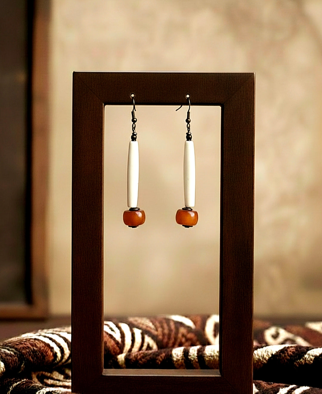 Pair of tube earrings displayed in a wooden frame with a blurred background