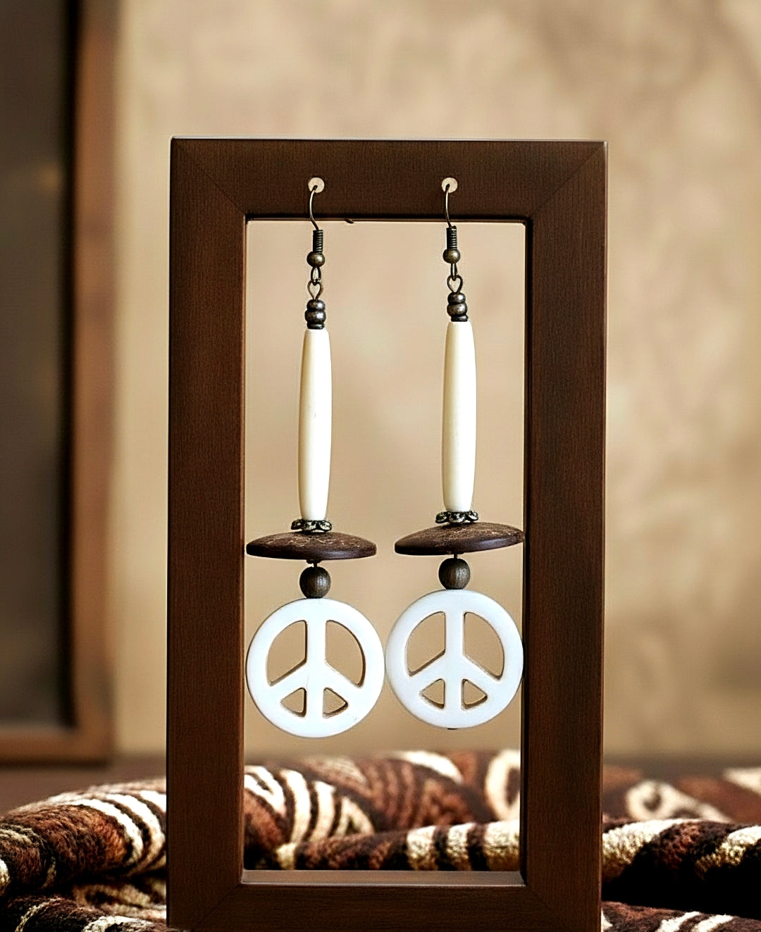 Peace sign earrings displayed in a wooden frame with a neutral background
