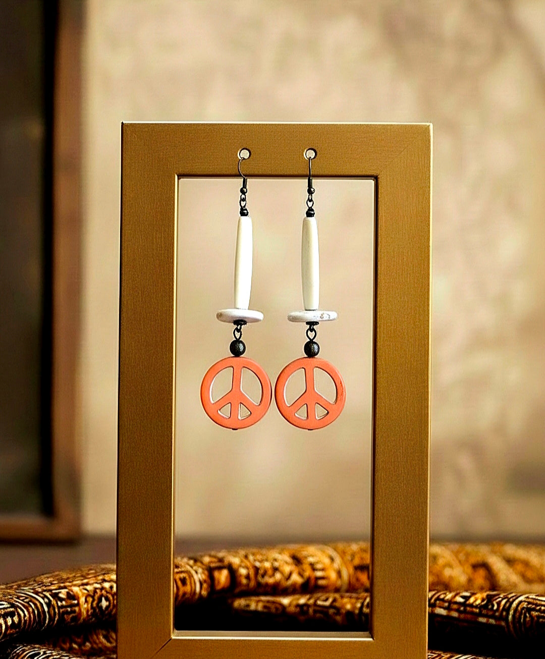 Peace sign earrings displayed in a gold frame against a neutral background