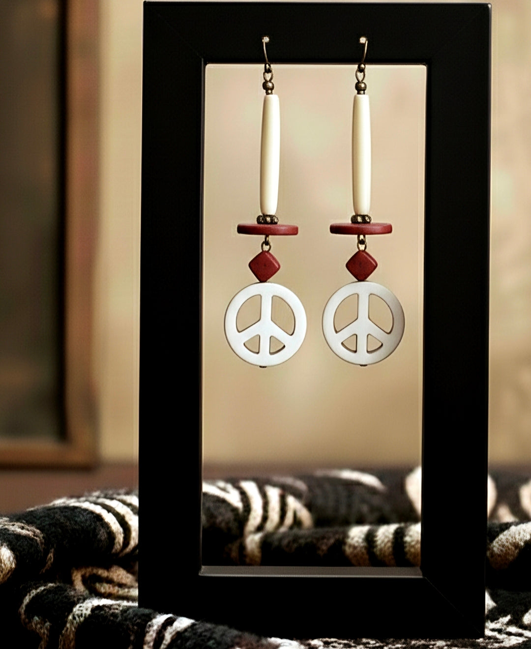Peace sign earrings with red accents on a black stand against a neutral background