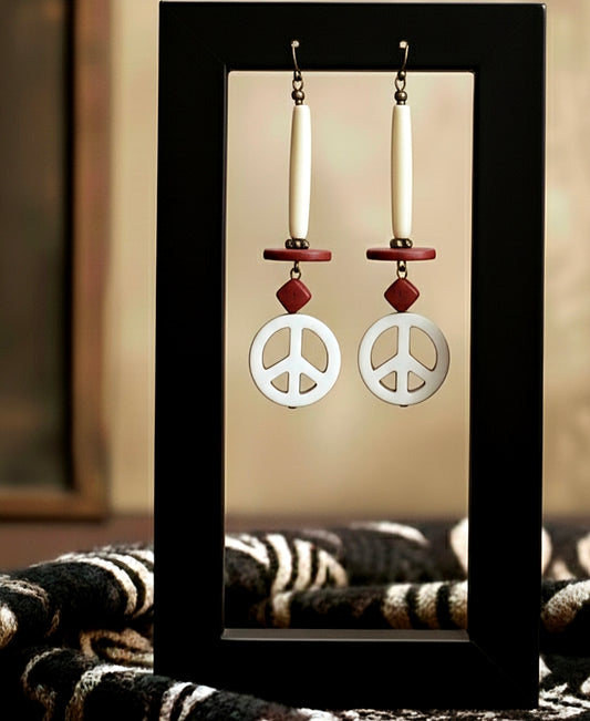 Peace sign earrings with red accents on a black stand against a neutral background