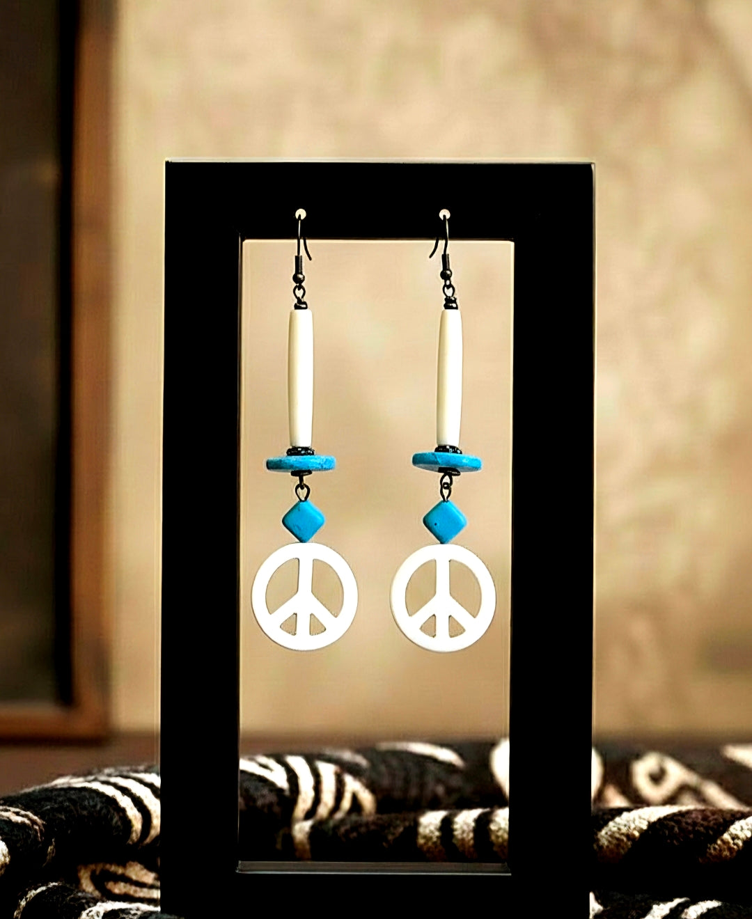 Peace sign earrings with blue accents on a black stand against a neutral background