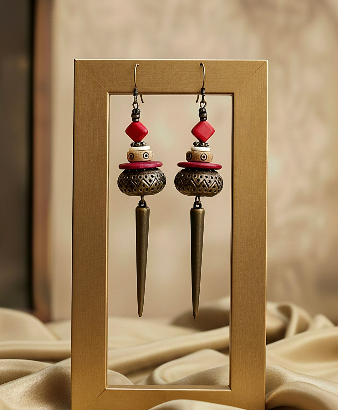Pair of ornate earrings with red and brass elements displayed in a frame.
