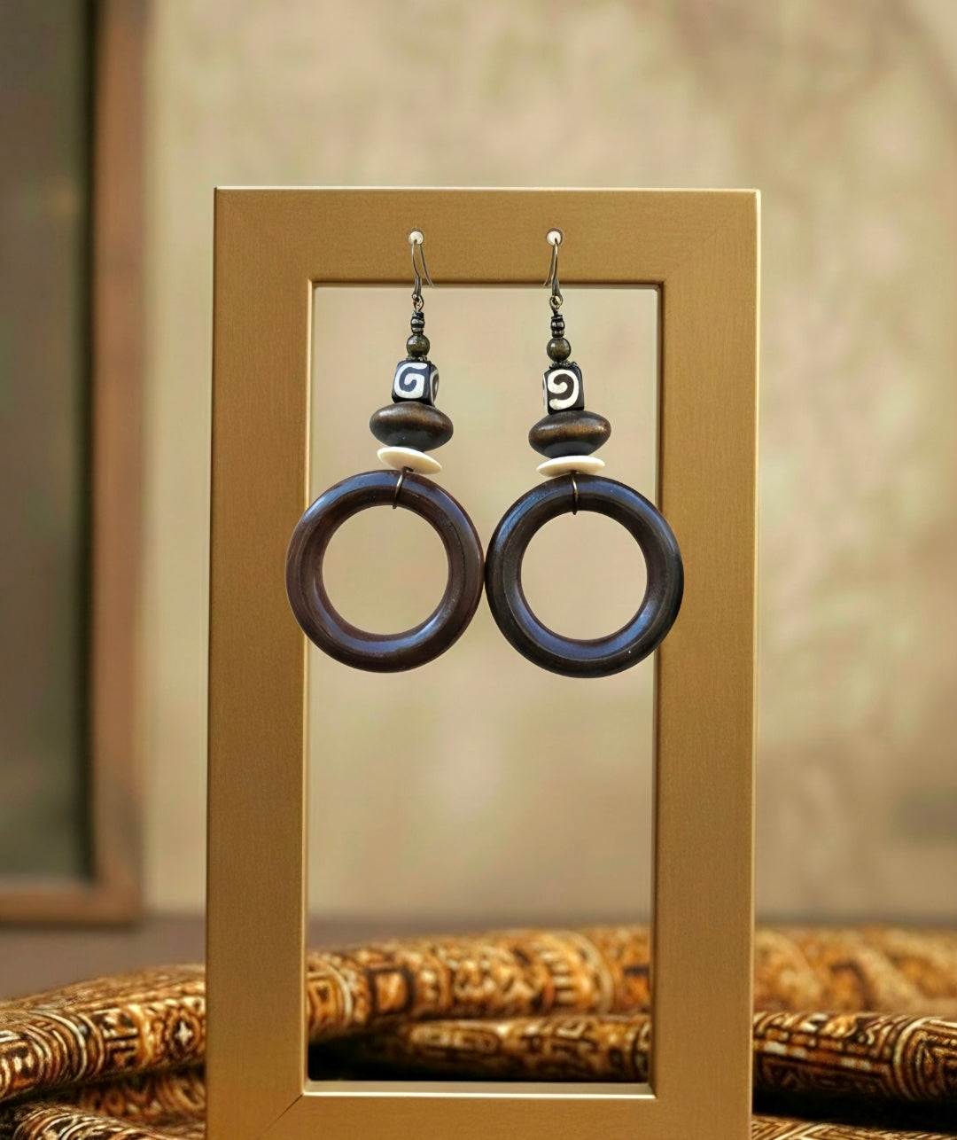 Pair of dark wooden hoop earrings hanging on a gold frame with a blurred background.