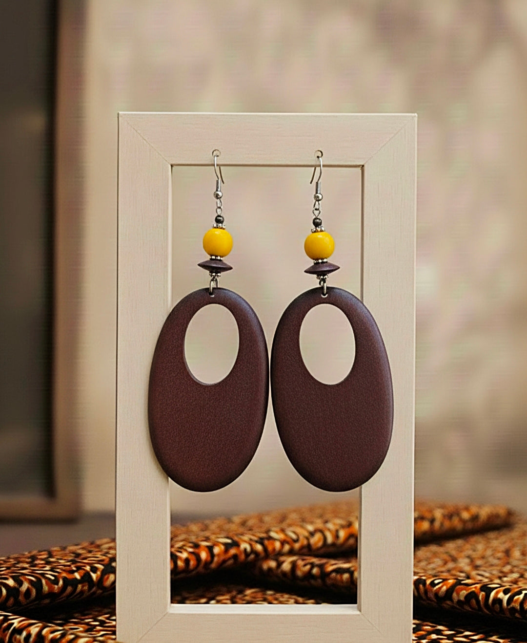 Pair of earrings with brown oval shapes and yellow beads on a neutral background