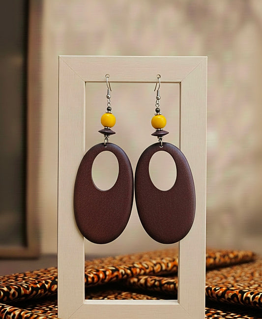 Pair of earrings with brown oval shapes and yellow beads on a neutral background