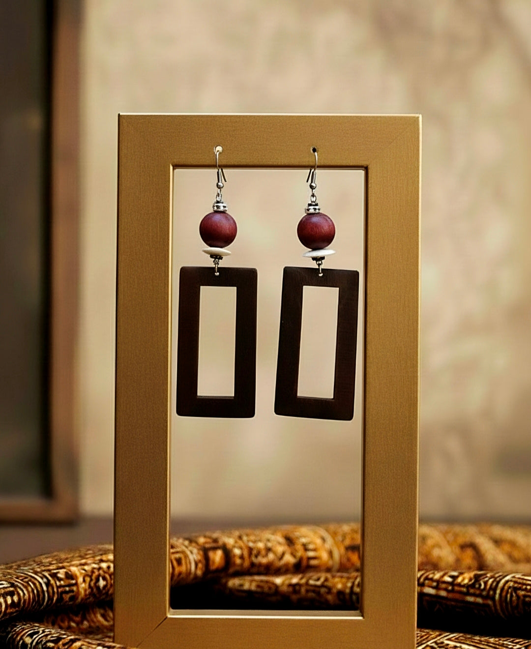 Pair of earrings with plum beads and black rectangular charms displayed in a gold frame.