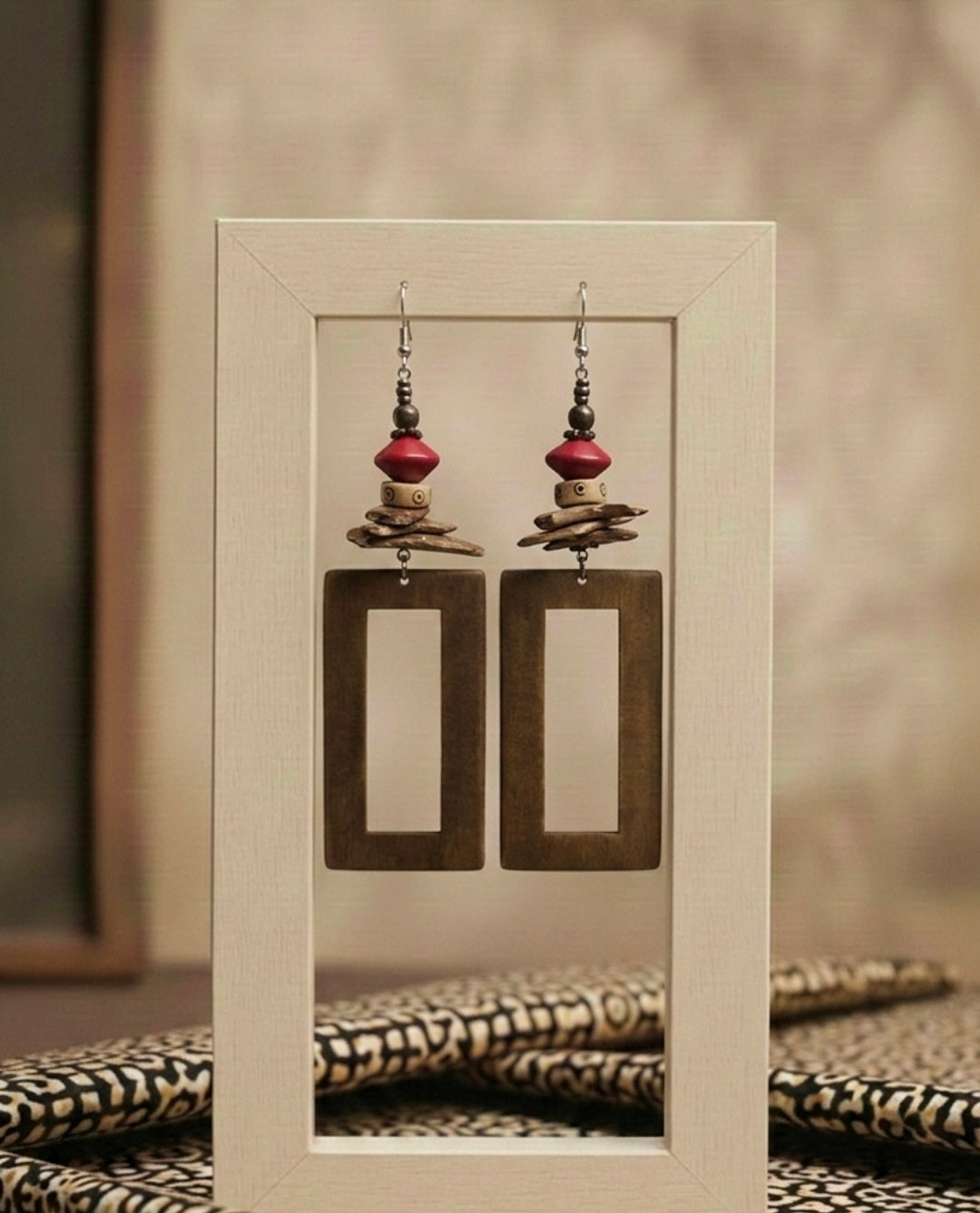 Pair of earrings with rectangular brown pendants and red beads in a clear display case.