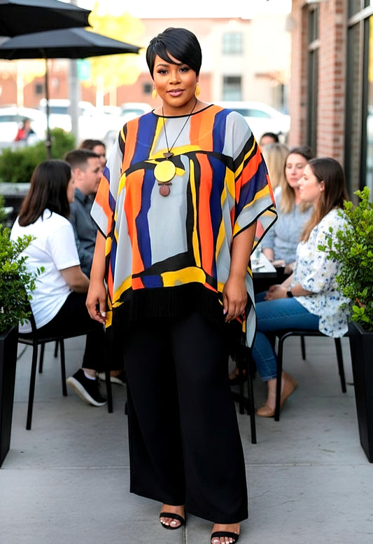 Woman in a colorful top and black pants standing outdoors with people in the background