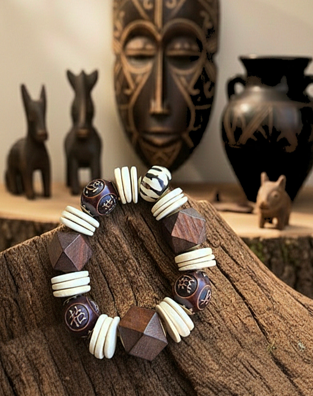 Bracelet with geometric beads on a wooden surface, with tribal masks and sculptures in the background.