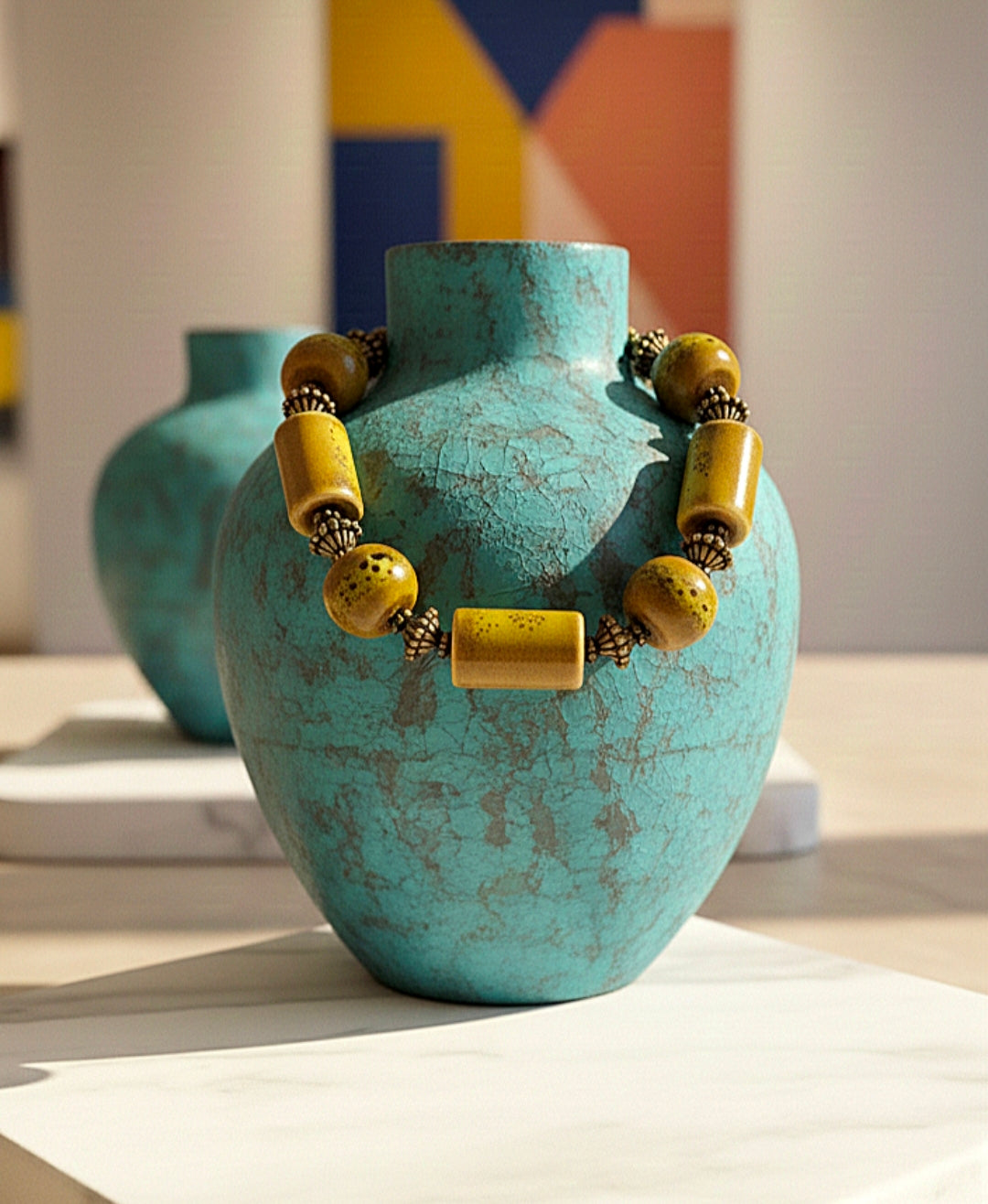 Turquoise vase with a bracelet made of yellow and gold beads on a light surface.