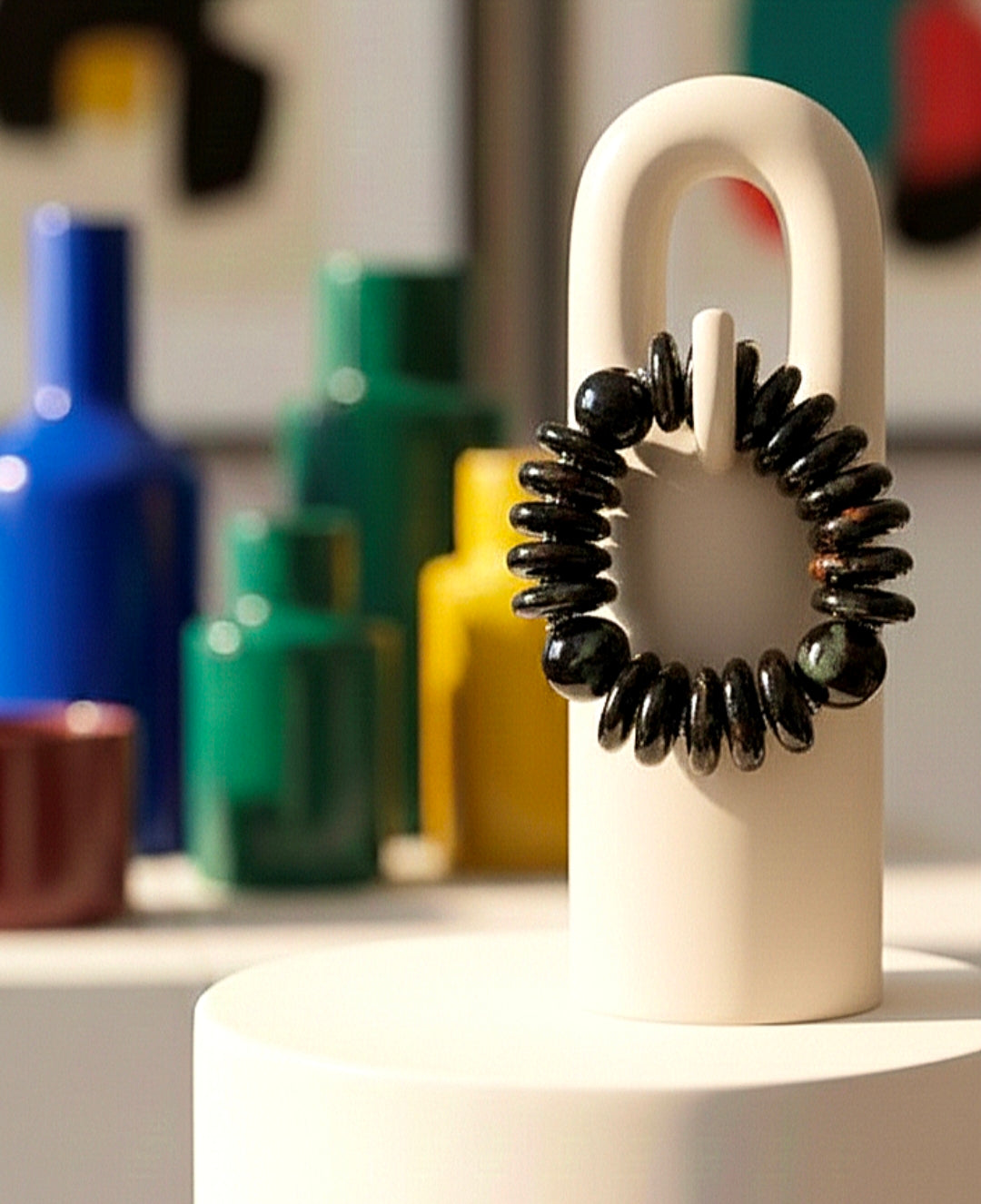 Black beaded bracelet on a white stand with colorful bottles in the background