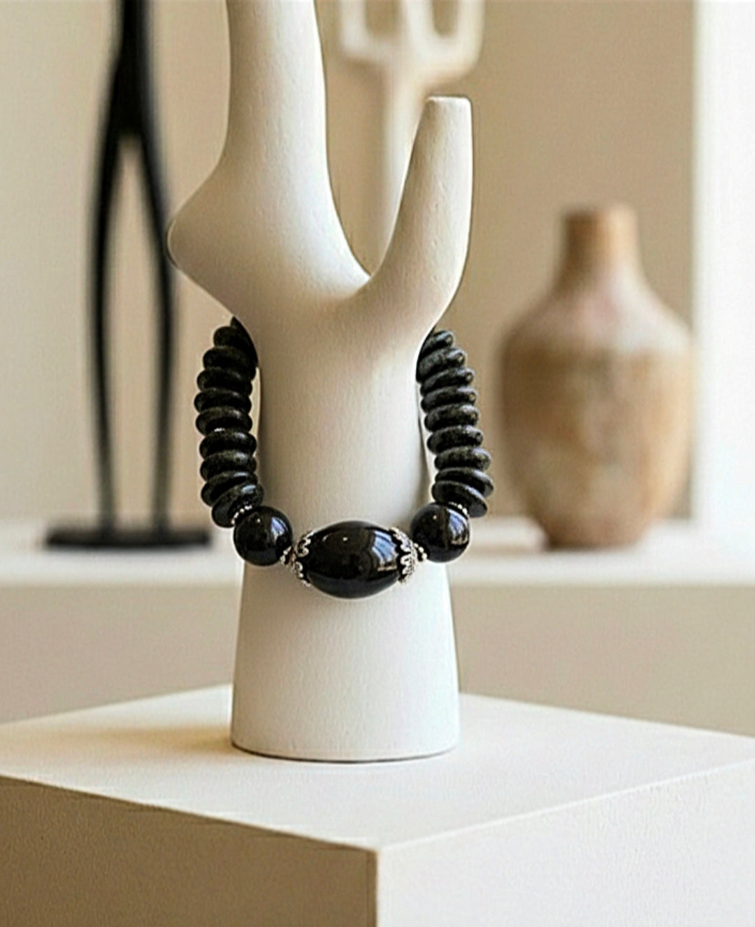 Black beaded necklace on a white ceramic stand with a neutral background