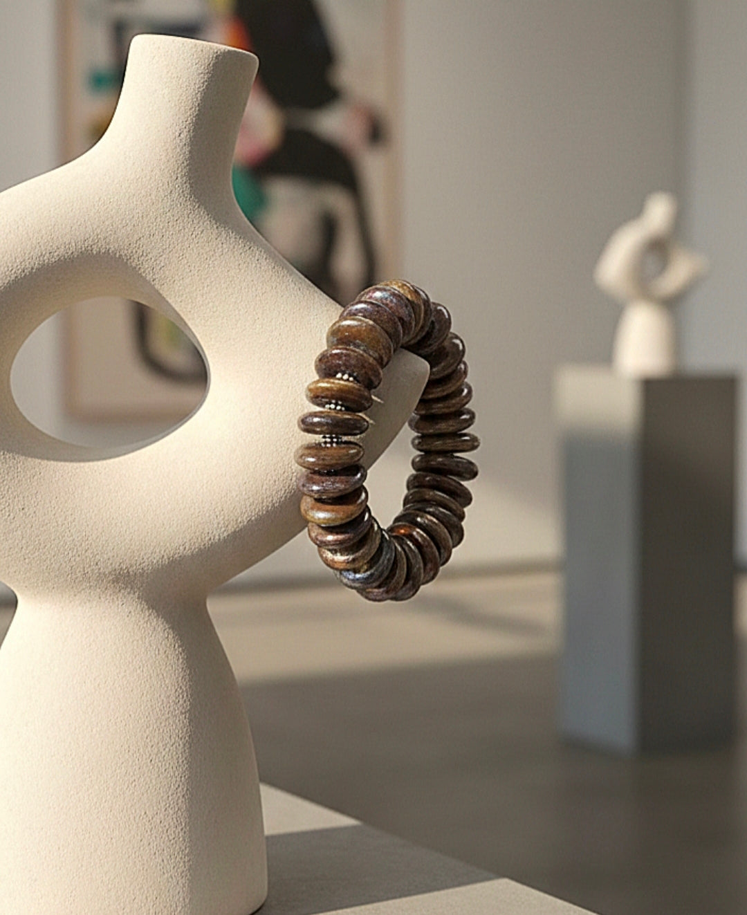 Brown beaded bracelet on a white abstract sculpture with a blurred indoor setting