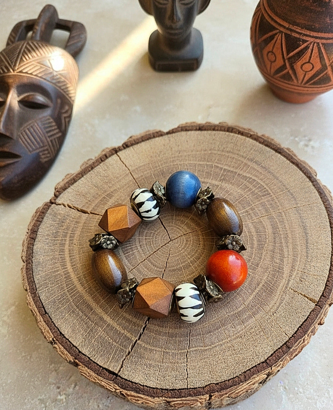 Colorful beaded bracelet on a wooden surface with decorative masks and pots in the background