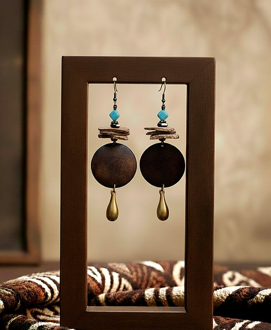Pair of earrings with wooden and other elements displayed in a wooden frame.