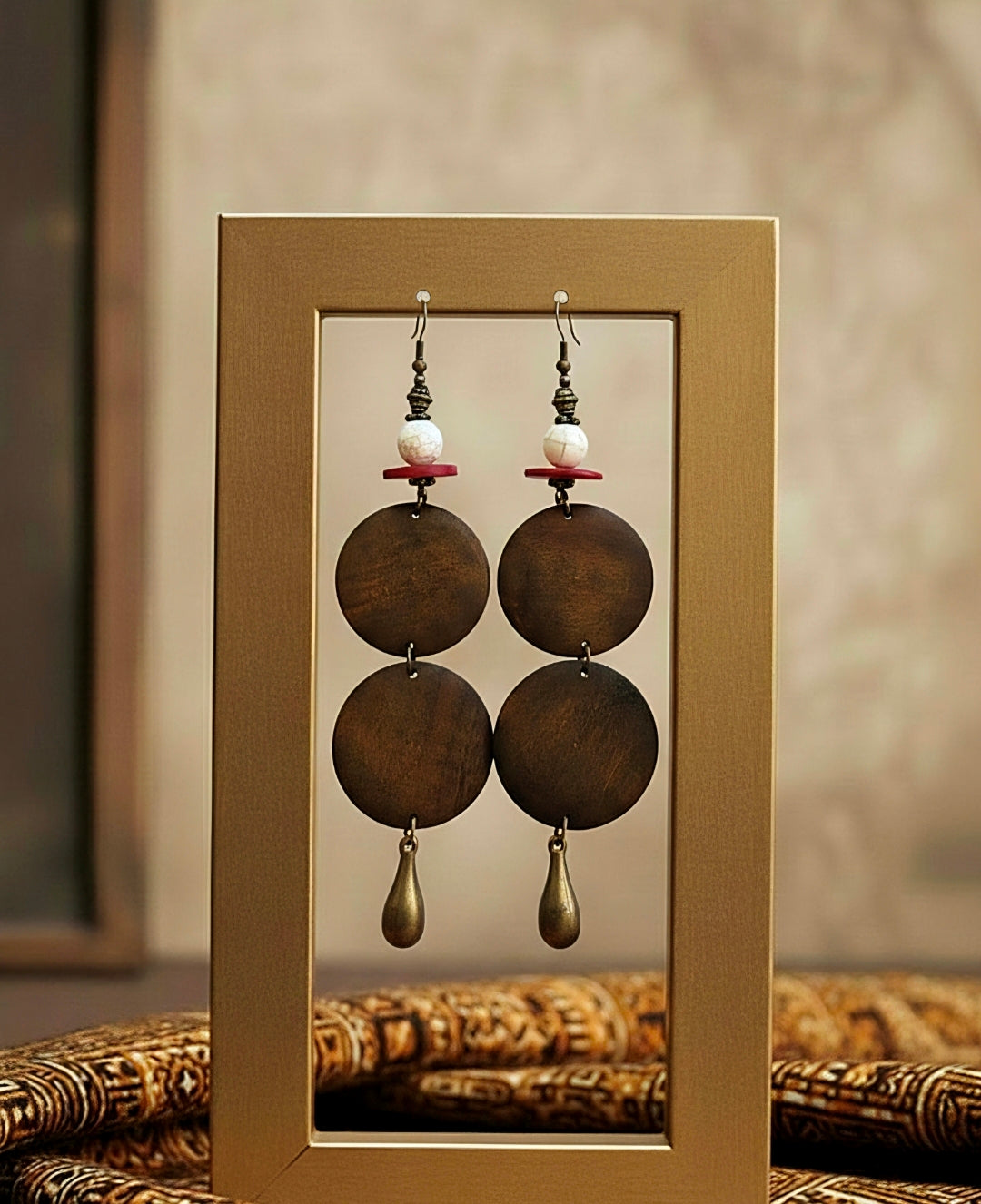 Pair of earrings with brown circular pendants and pearl beads displayed in a gold frame.