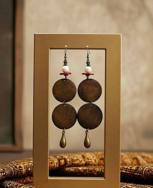 Pair of earrings with brown circular pendants and pearl beads displayed in a gold frame.