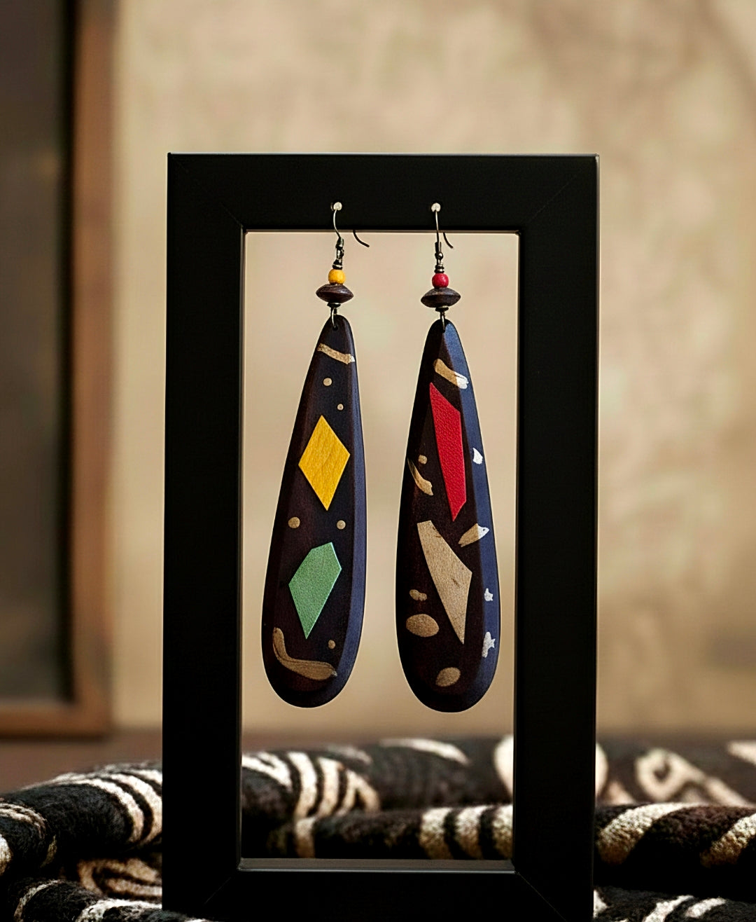 Pair of colorful earrings displayed in a black frame against a neutral background.