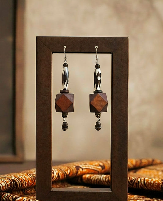 Pair of earrings with wooden and metallic components displayed in a wooden frame.