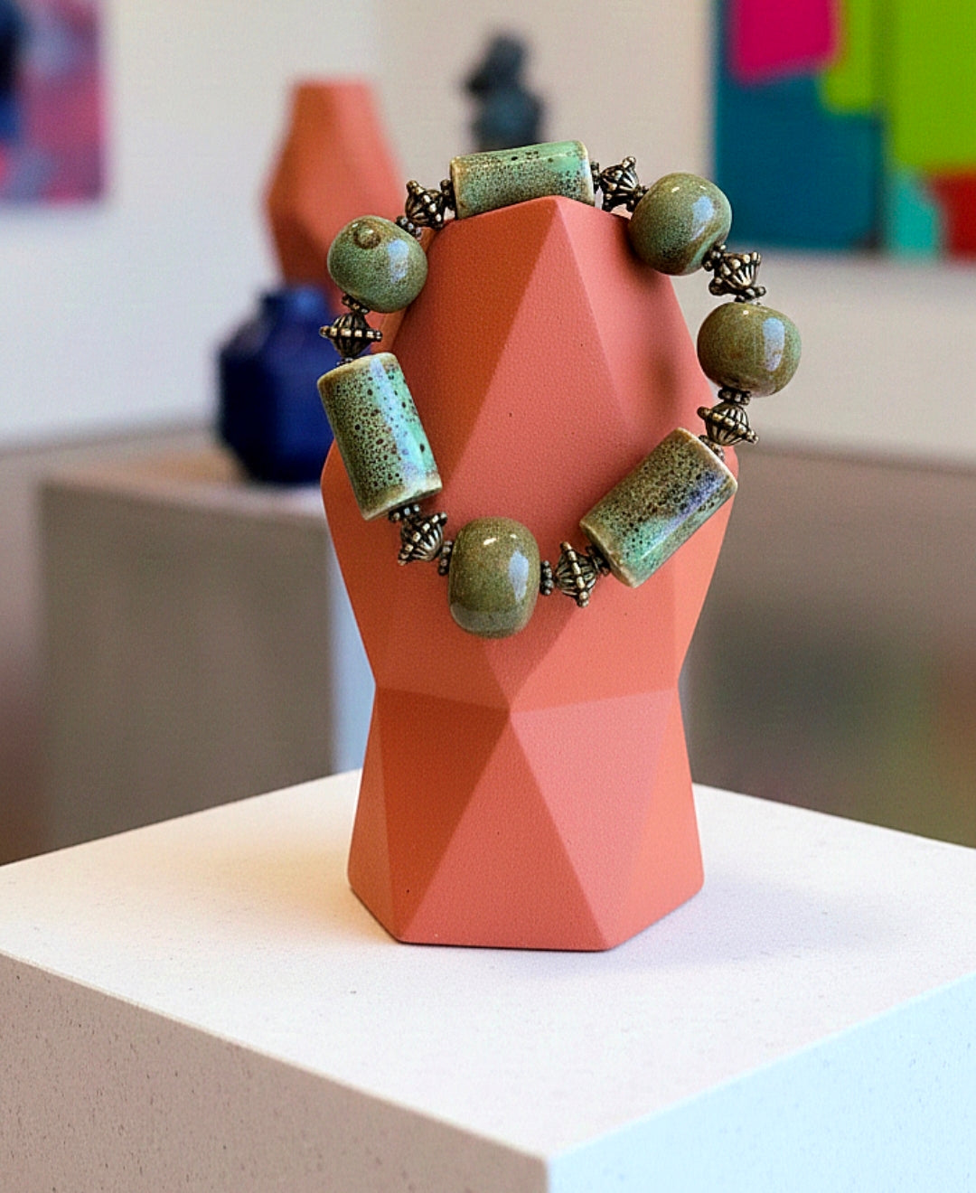 Bracelet with green beads on a pink geometric stand against a blurred indoor background