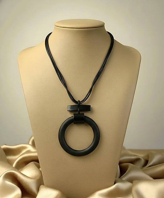 Black circular pendant necklace on a beige mannequin against a beige background