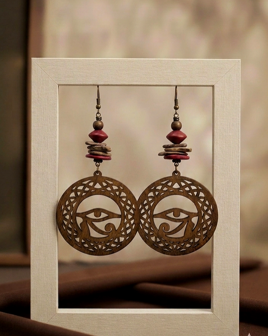 Pair of ornate earrings with eye design on a beige card.