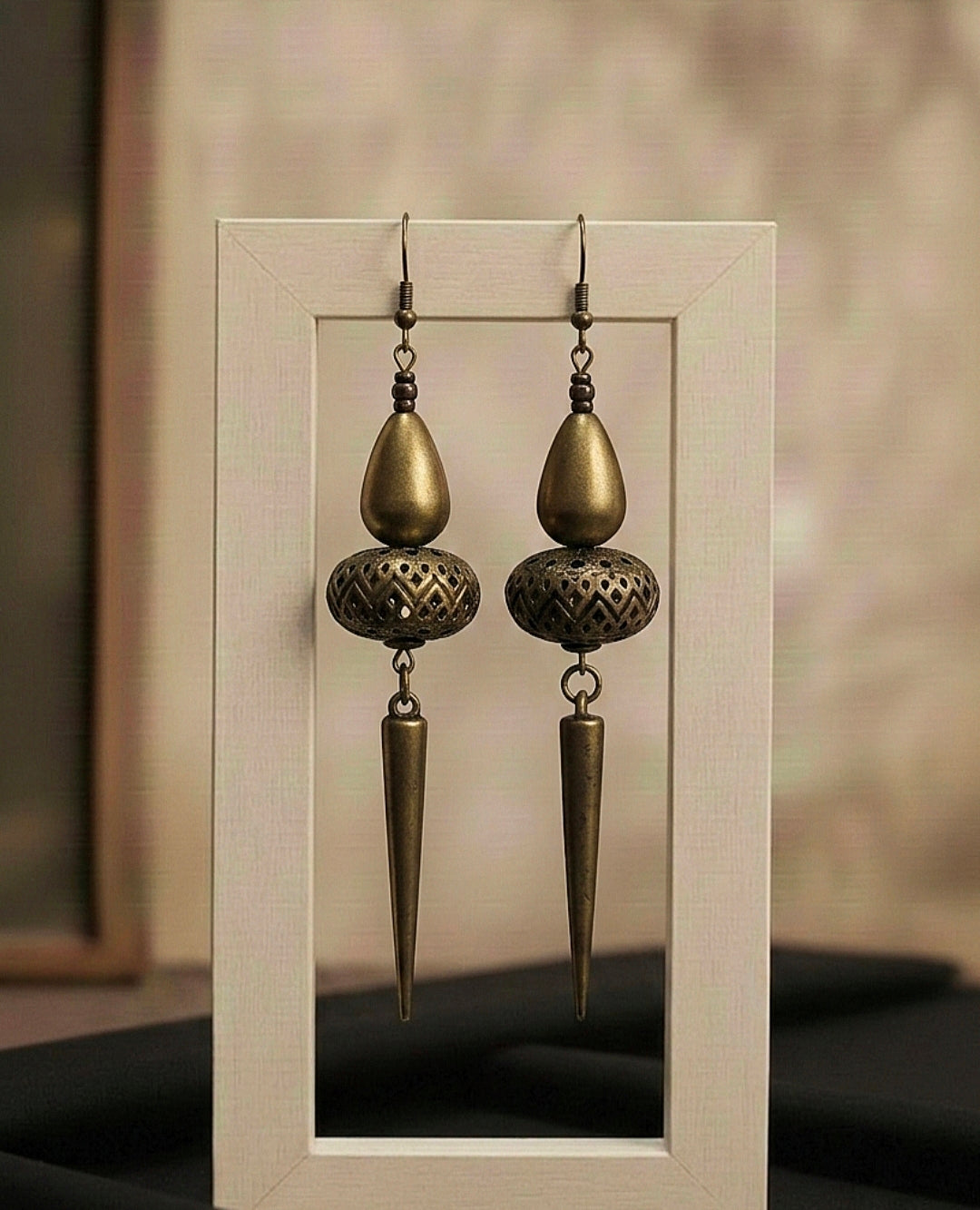 Pair of ornate bronze earrings hanging on a clear stand against a neutral background