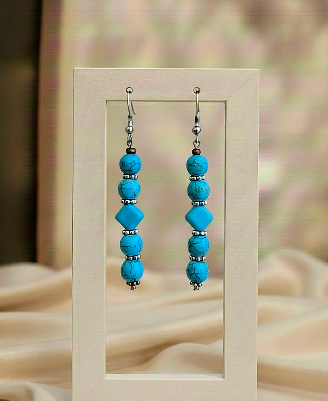 Turquoise beaded earrings on a beige stand with a blurred background