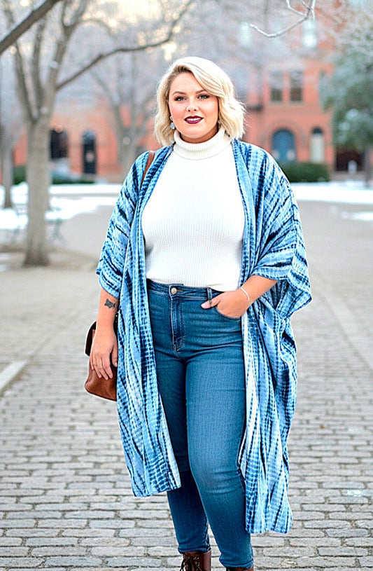 Woman wearing a blue plaid shawl over a white sweater and blue jeans on a brick sidewalk.
